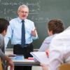 Teacher stands in front of a chalkboard with mathematical equations as he speaks to high school students.